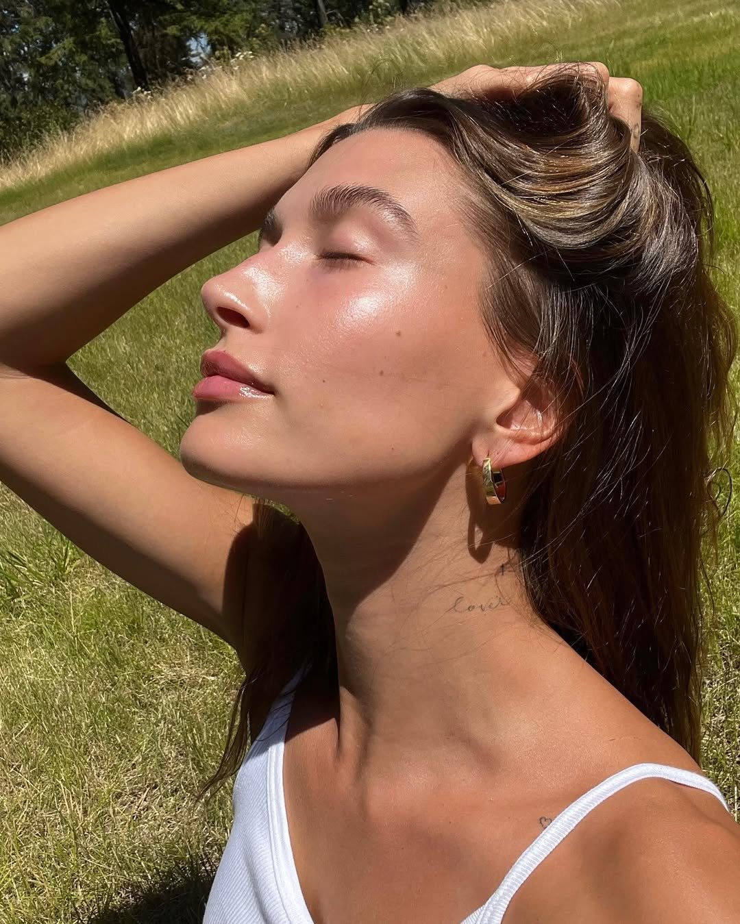 Hailey Bieber em um campo ensolarado, com pele brilhante e refletindo saúde, conhecido como 