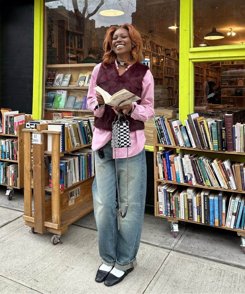 Pessoa vestindo camisa rosa e colete marrom lê em frente a estante de livros, mostrando como usar sobreposições.
