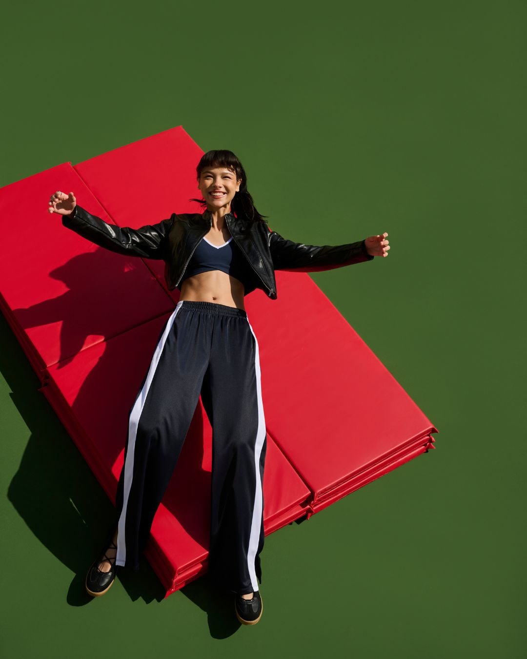 Pessoa sorrindo deitada em tapetes vermelhos, vestindo jaqueta de couro preta e calça esportiva, como ficar chique e confortável