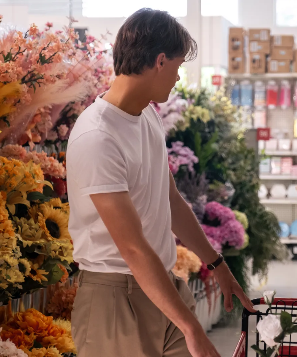 Jovem de camiseta branca empurrando carrinho em seção de flores.
