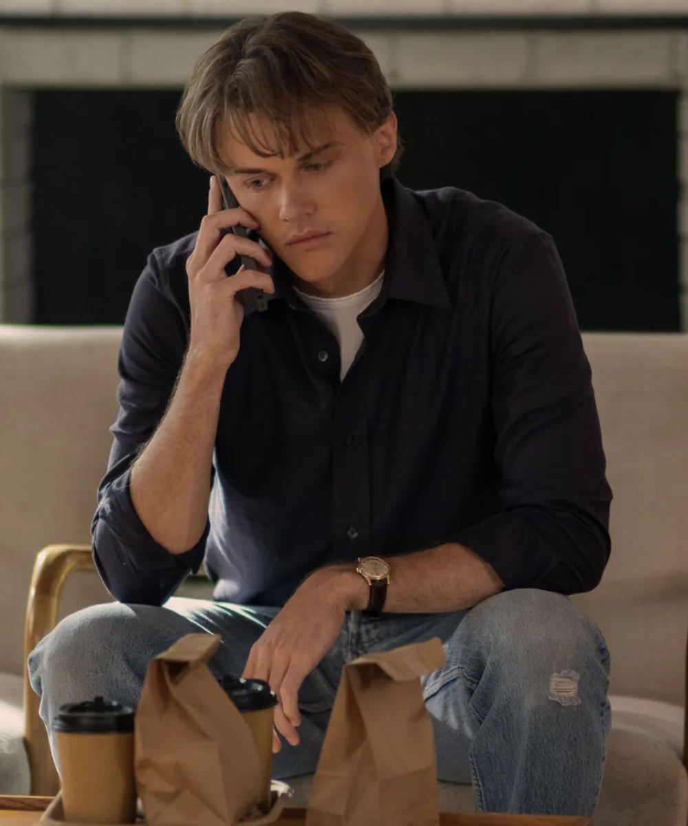 Conrad Fisher fala ao telefone sentado em um sofá, com sacos de papel e café na mesa.