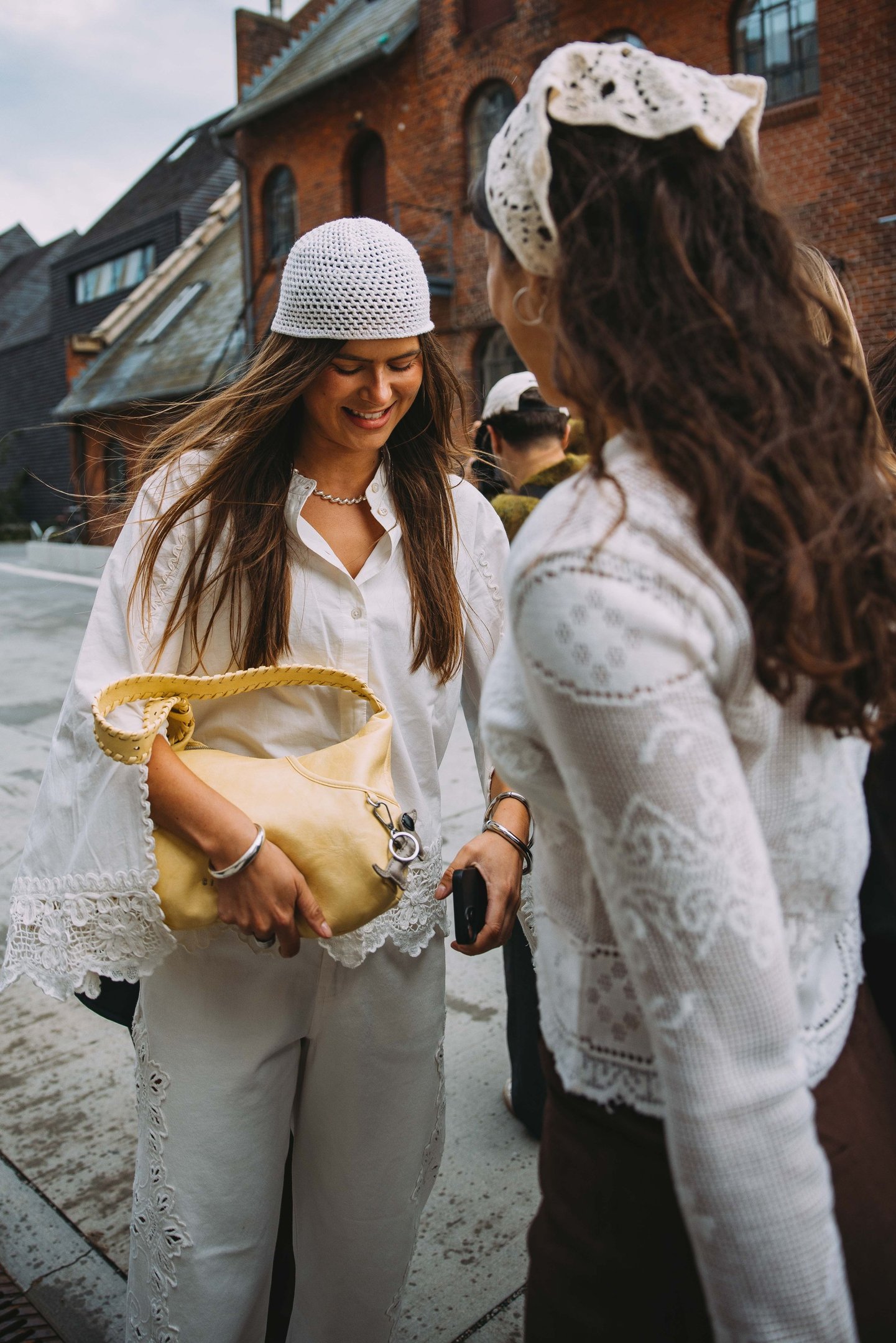 Duas mulheres conversando, uma usando touca de crochê branca e segurando uma bolsa amarela.