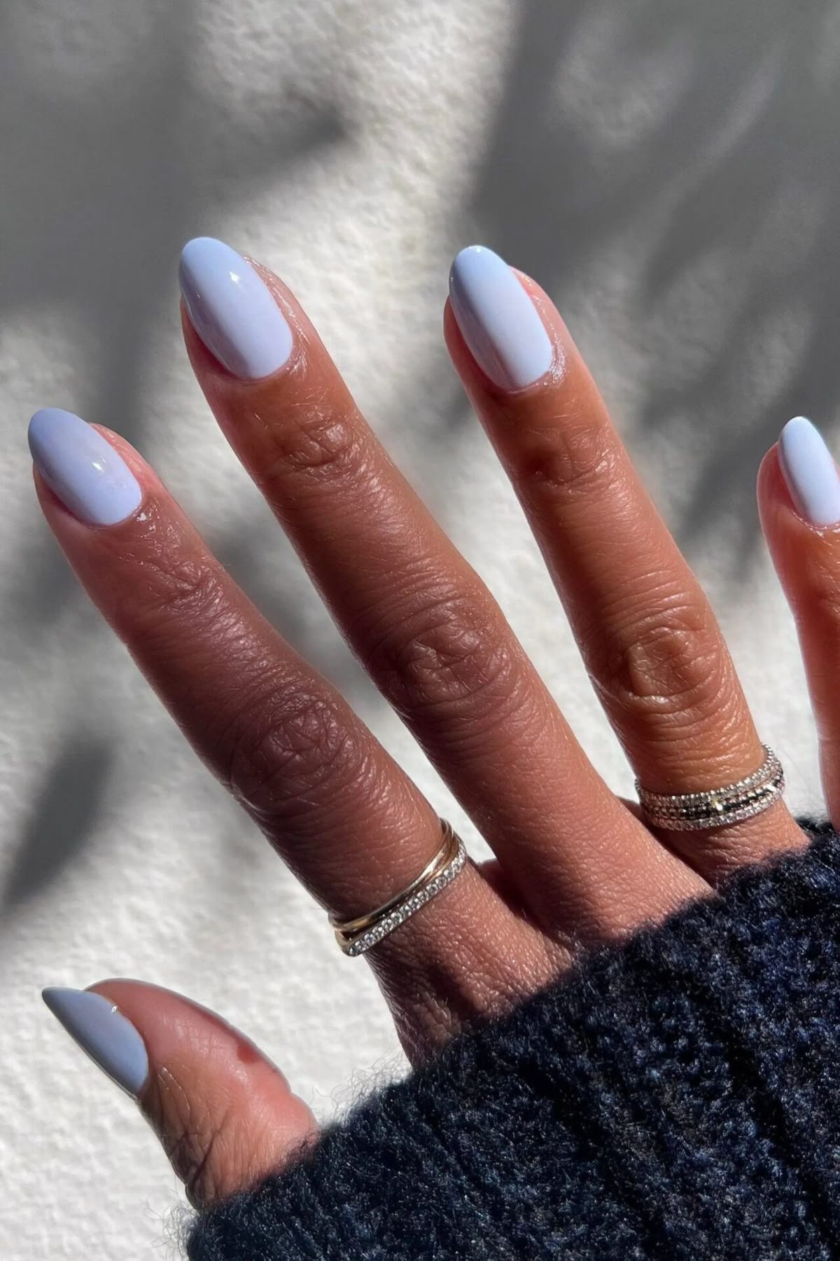 Unhas pintadas de lilás claro, acompanhadas por anéis prateados, tendência nas cores de esmalte 2025.