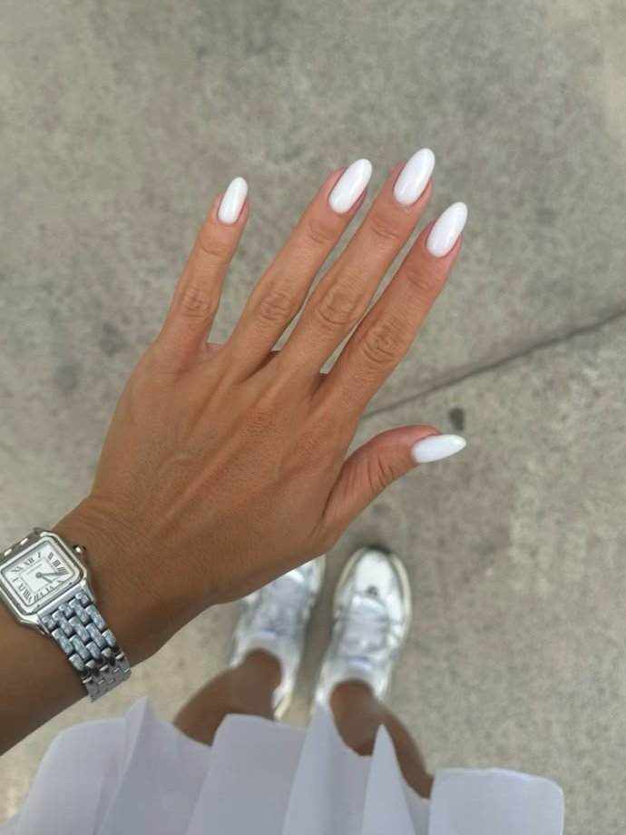 Unhas com esmalte branco perolado e anel de relógio prateado no pulso, refletindo tendências de cores de esmalte 2025.