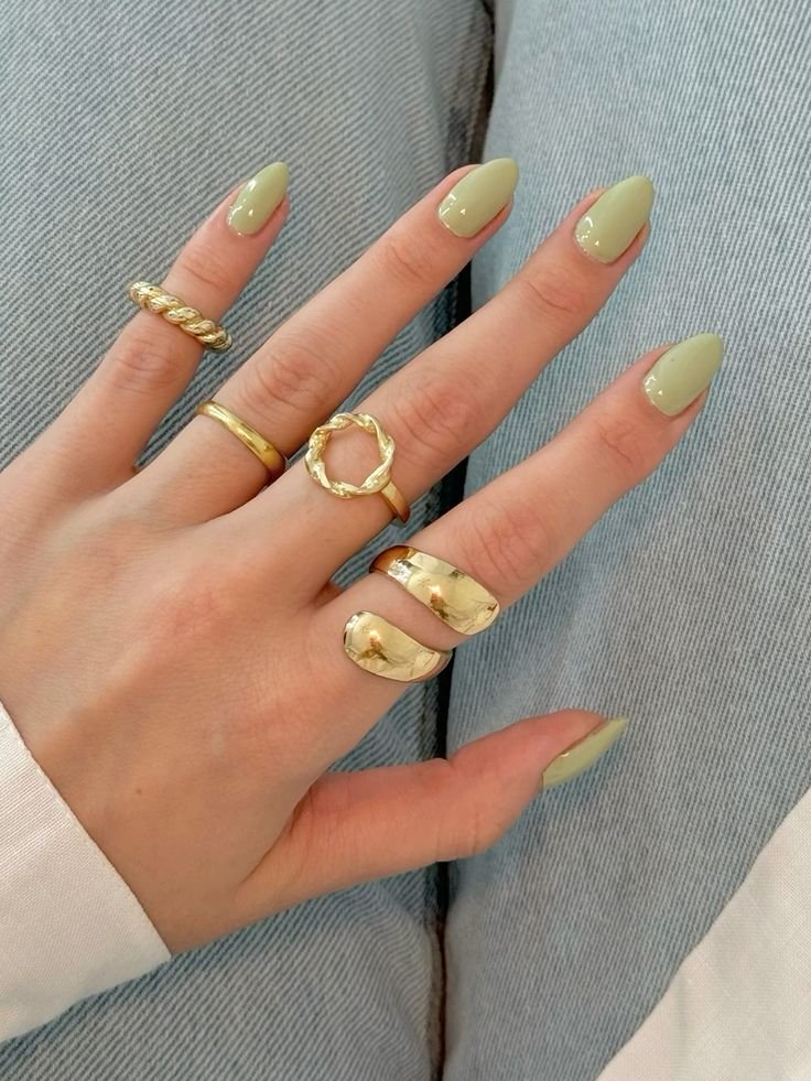 Unhas com esmalte verde claro e vários anéis dourados. Ideal para inspirar cores de esmalte 2025.