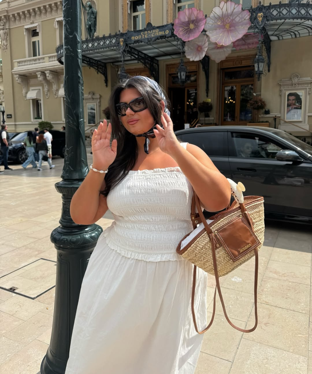 Mulher com vestido branco e bolsa de palha, posando em frente ao Cassino de Monte Carlo. Cores do verão 2026.