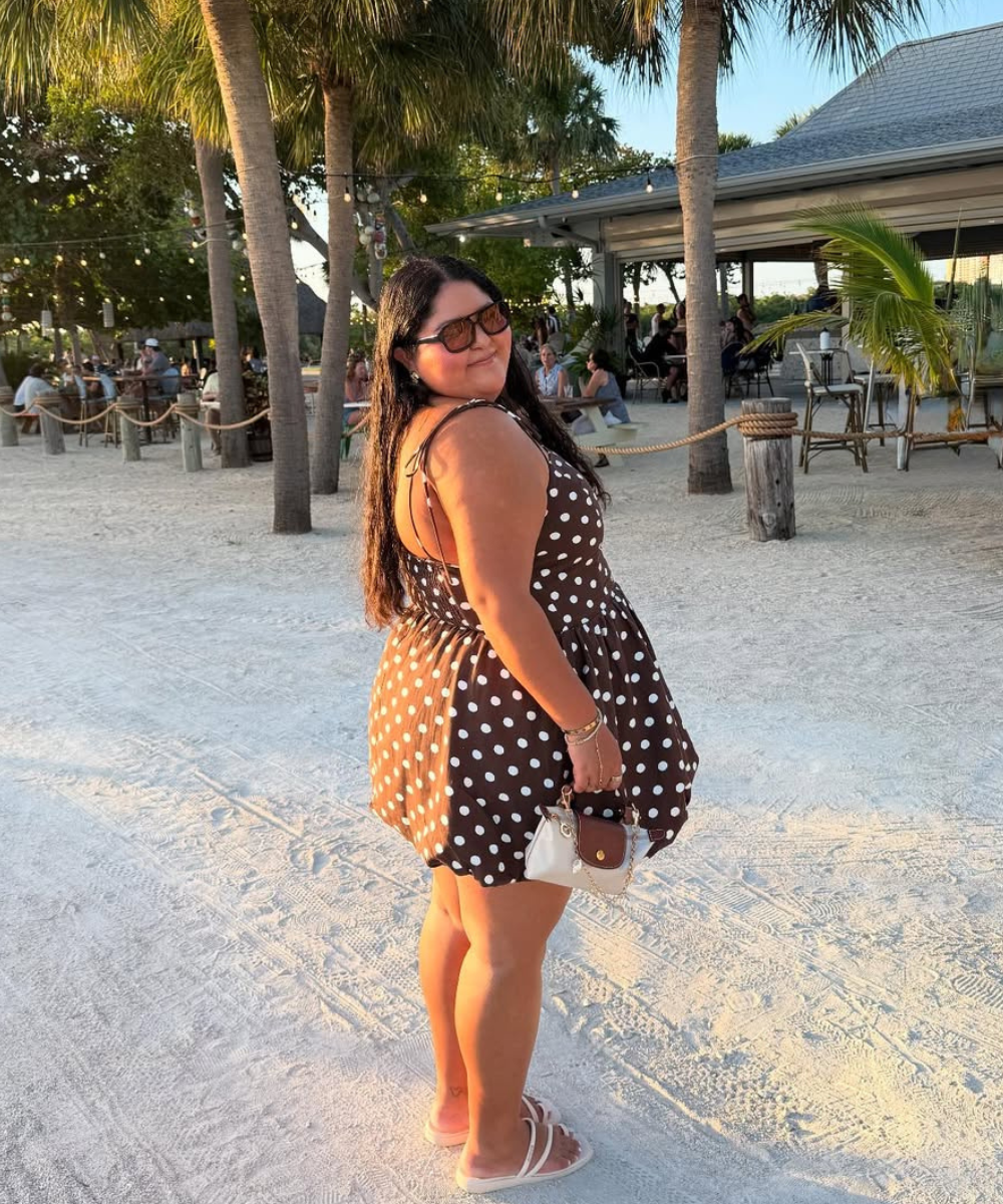 Praia com palmeiras e mulher de óculos em vestido marrom de bolinhas. Ambientes como este destacam as cores do verão 2026.