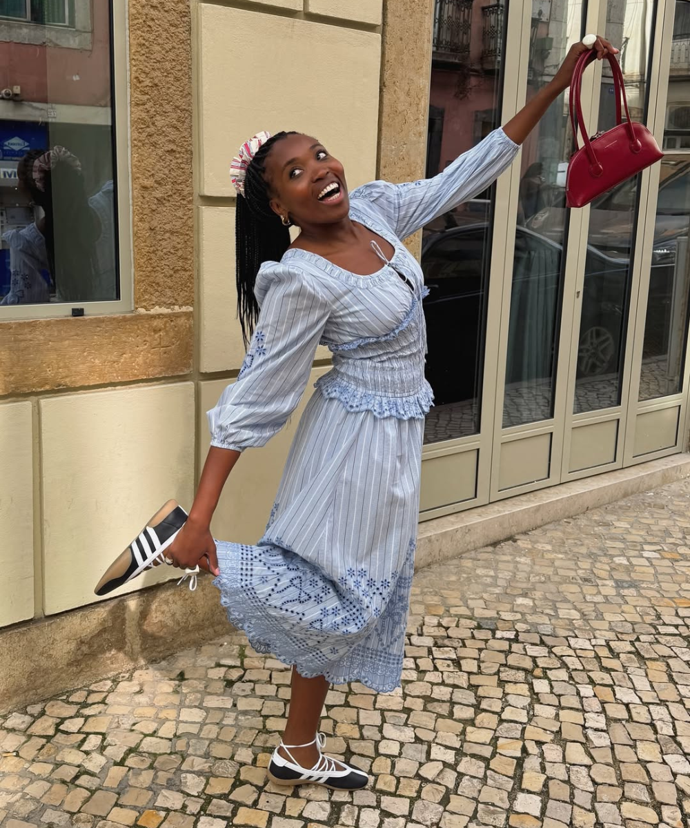 Pessoa sorrindo em um vestido azul claro floral, segura uma bolsa vermelha ao ar livre. Cores do verão 2026.
