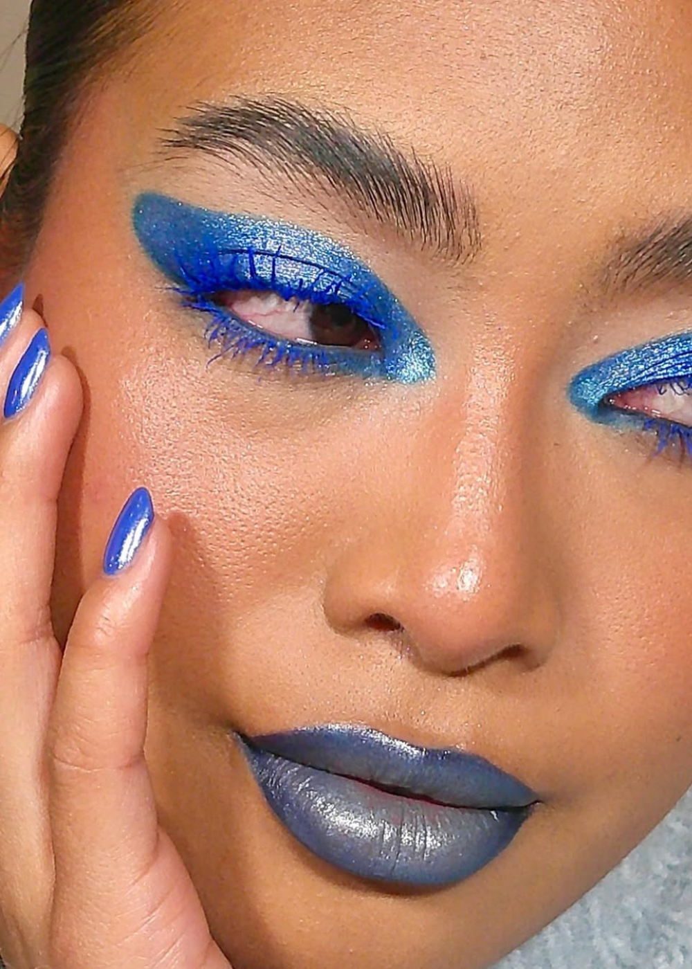 Maquiagem vibrante em azul cobalto nos olhos, lábios e unhas, destacando um visual ousado e artístico.