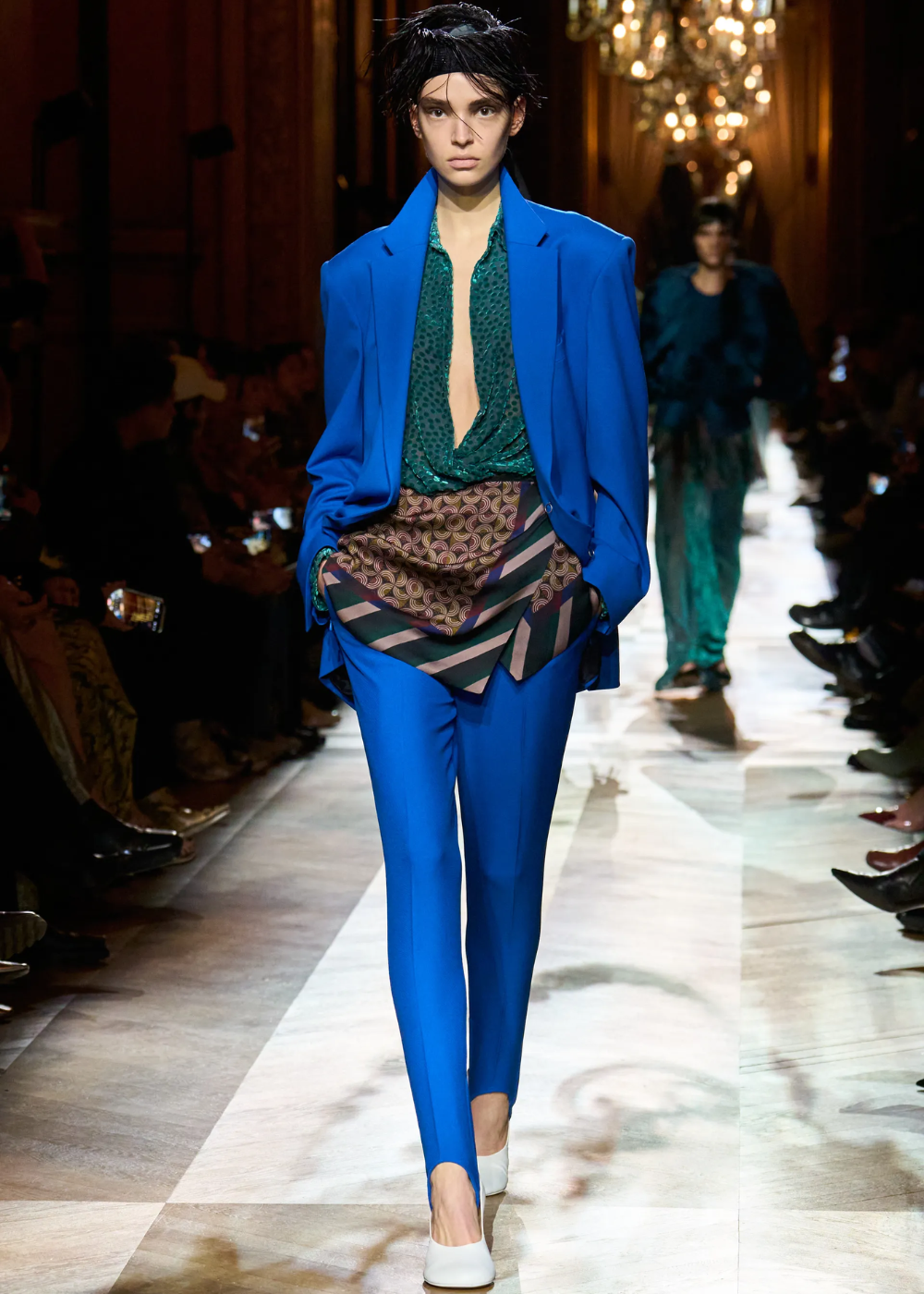 Modelo em passarela usando terno azul cobalto vibrante, blusa verde e saia estampada geométrica.