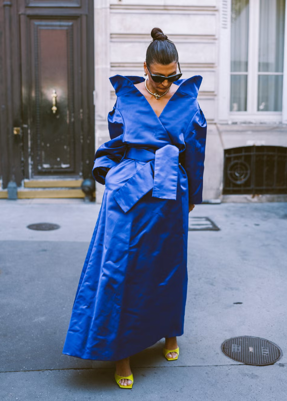 Vestido longo azul cobalto com ombreiras, usado por pessoa com óculos escuros e sandálias amarelas em ambiente urbano.