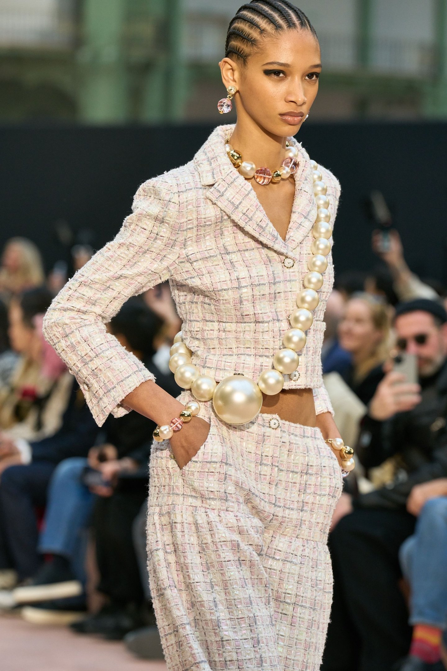 Modelo com terno texturizado e colar de pérolas grandes na passarela do fashion month.