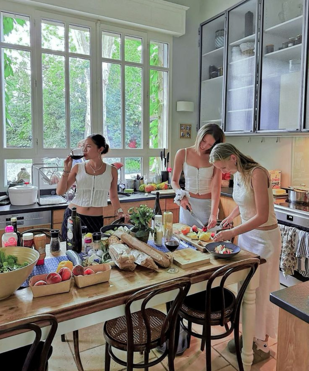 Grupo de amigos adultos preparando uma refeição juntos em uma cozinha bem iluminada.