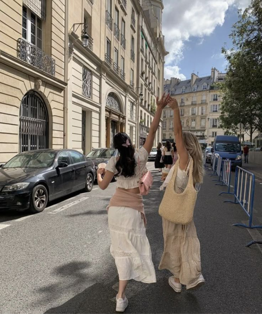 Amigas caminhando de mãos dadas em rua ensolarada, representando amizade na vida adulta.
