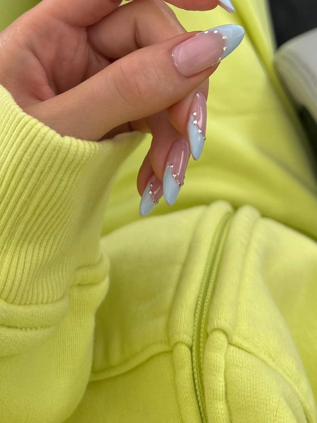 As unhas, em formato amendoado, têm acabamento azul claro, decoradas com pequenos pontos prateados.