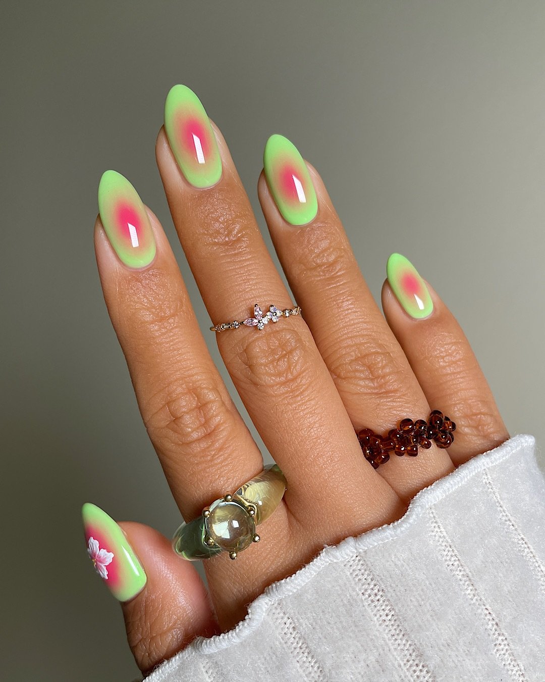 Unhas decoradas em tons de verde e rosa com anéis, representando estilo tropical guava girl.