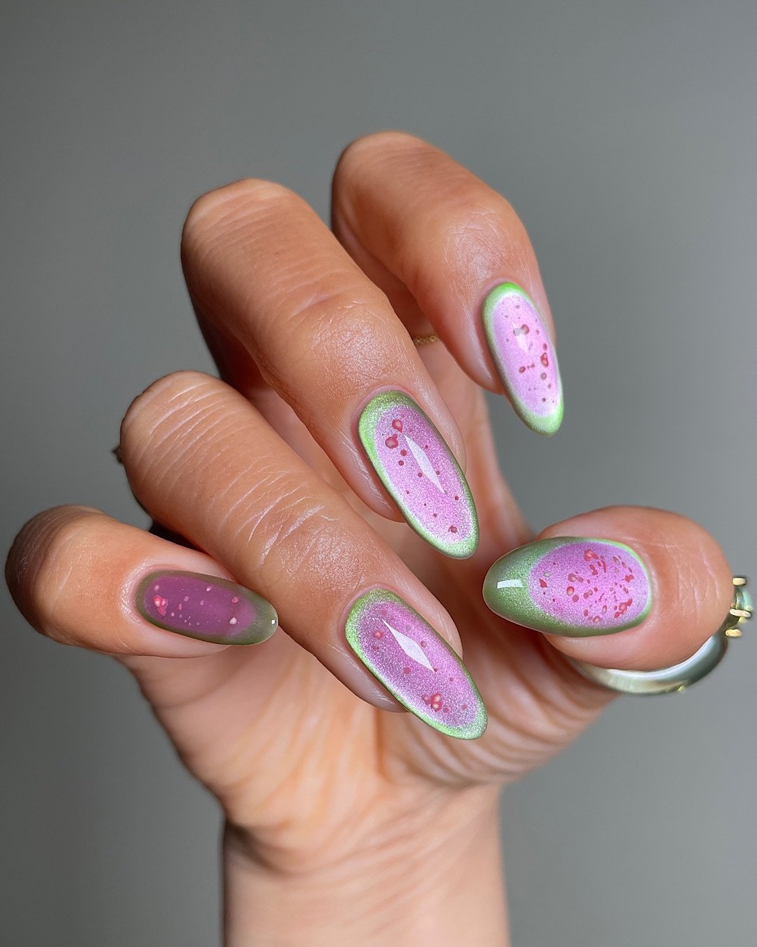 Unhas decoradas com esmalte rosa e verde, inspiradas em guavas, com detalhes delicados em vermelho.