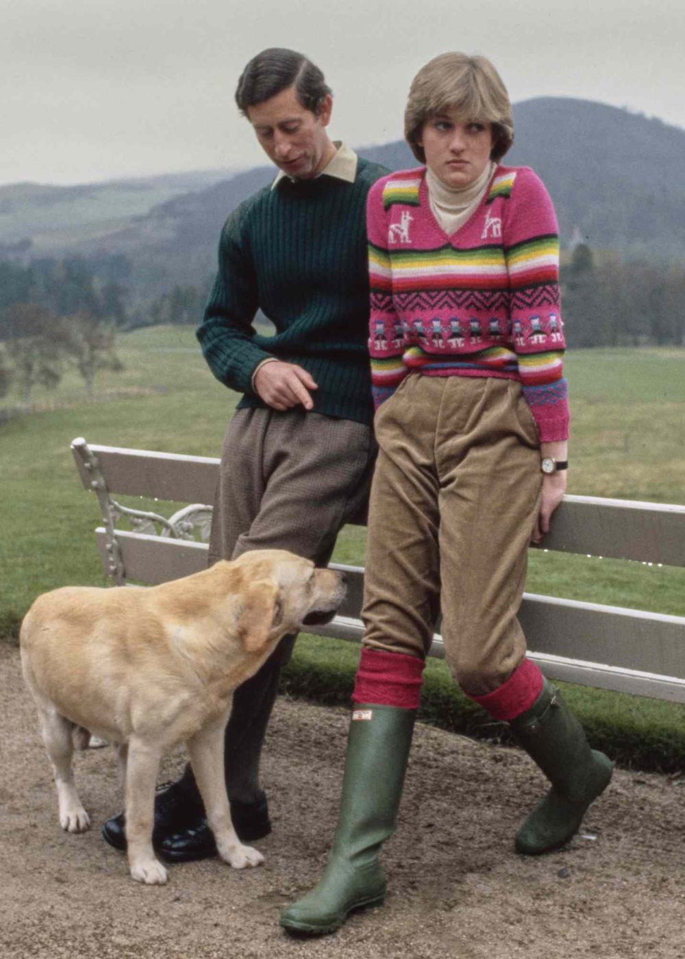 Dois indivíduos e um cão em um campo, com um deles usando botas de chuva Hunter verdes.