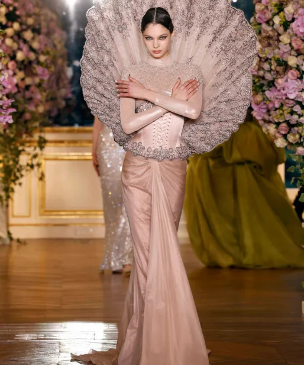 Modelo usando vestido elegante com estrutura ornamentada, estilo Schiaparelli, em ambiente luxuoso com flores.