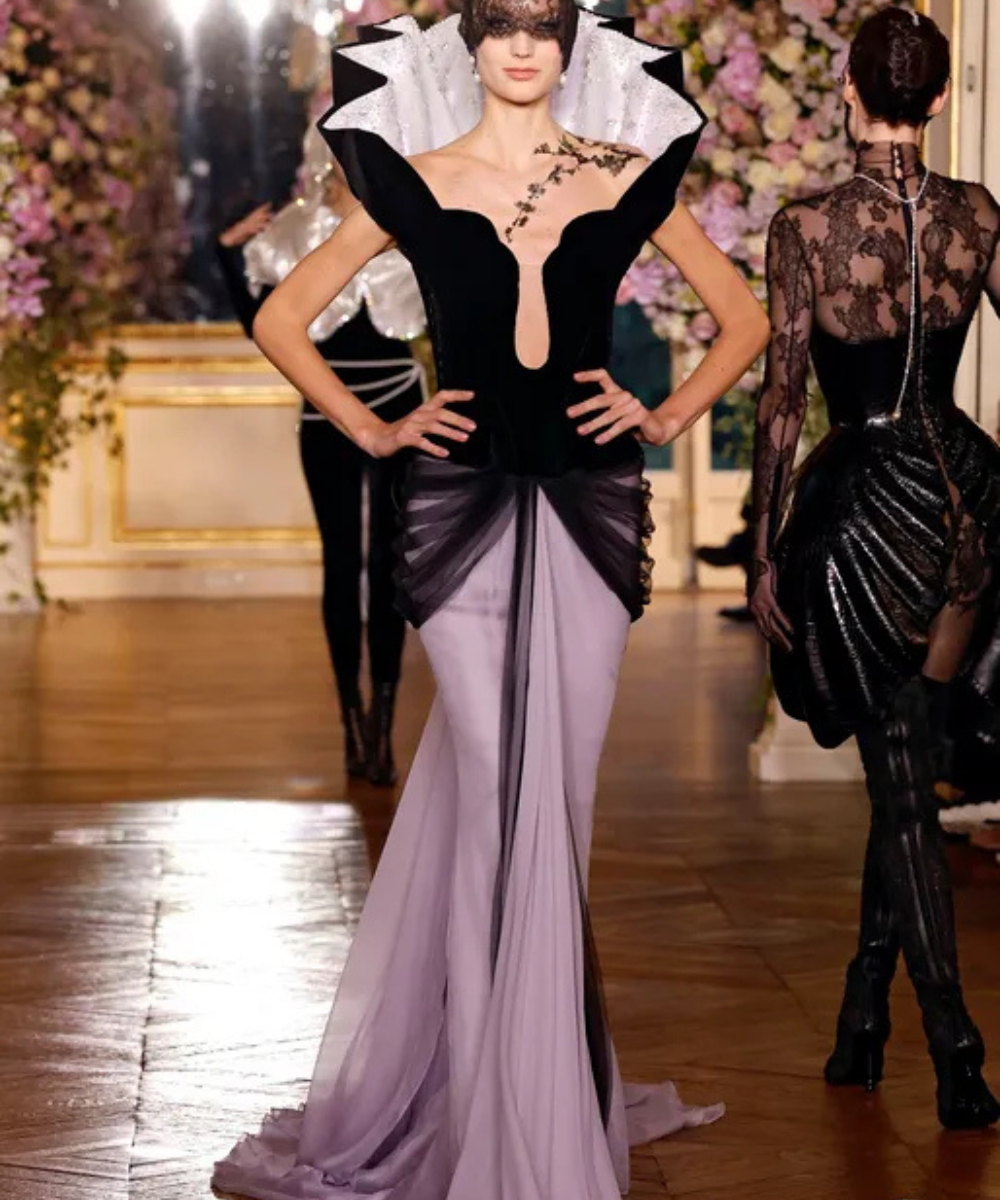 Modelo em passarela com vestido couture sofisticado, destacando design arquitetônico com preto e lilás, estilo Schiaparelli.