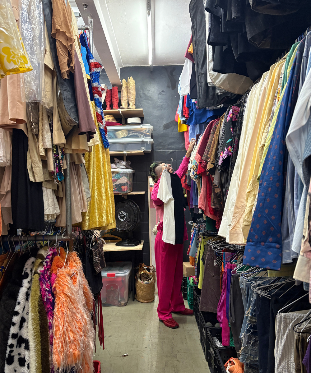 Pessoa em um estoque de roupas variadas, explorando um local cheio de peças vibrantes e 