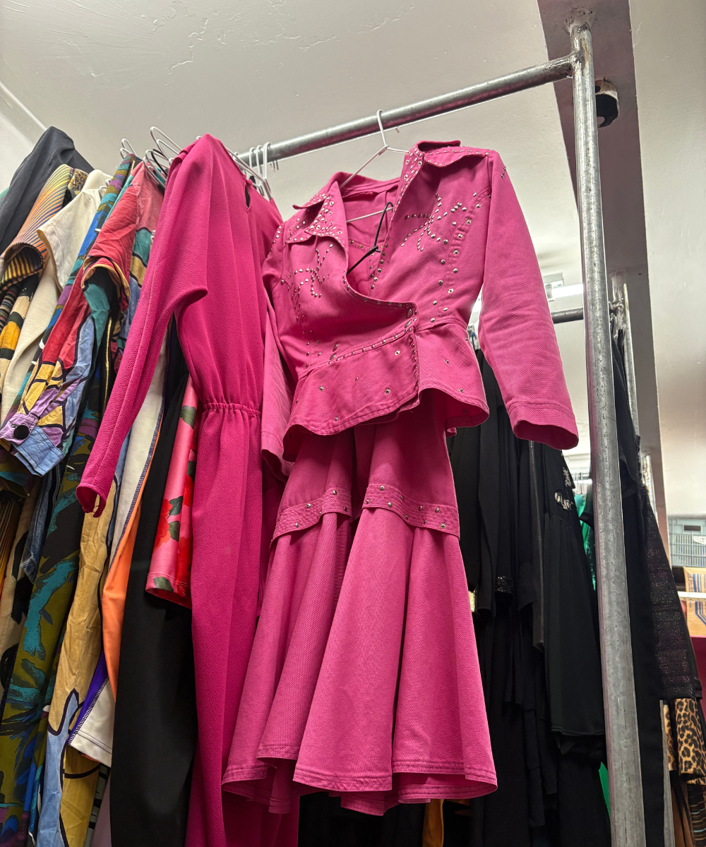 Conjunto rosa vibrante, decorado com tachinhas prateadas, pendurado junto a outras roupas em várias cores.