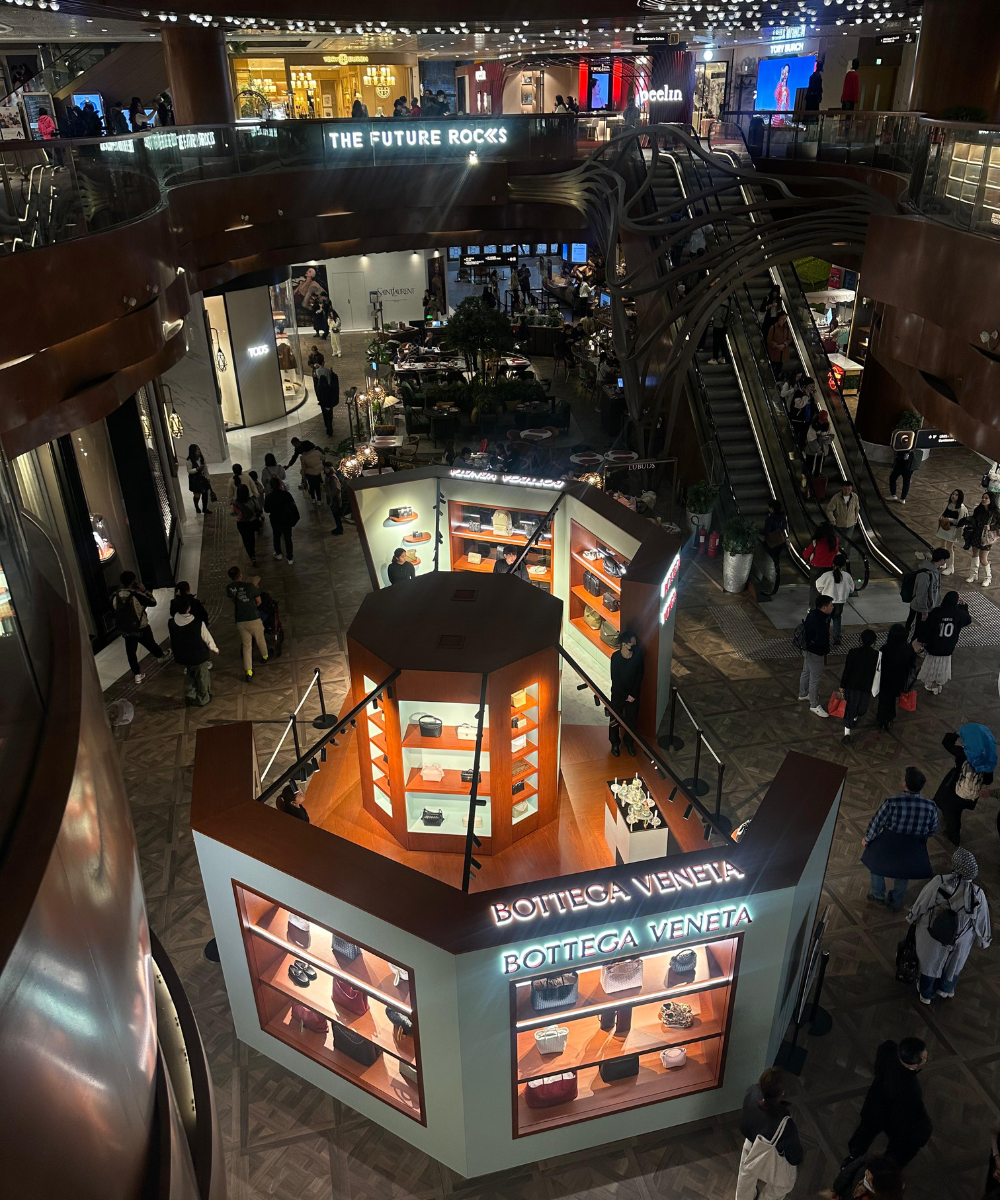 Shopping movimentado na Ásia com loja Bottega Veneta em destaque, cercada por visitantes e estrutura moderna.