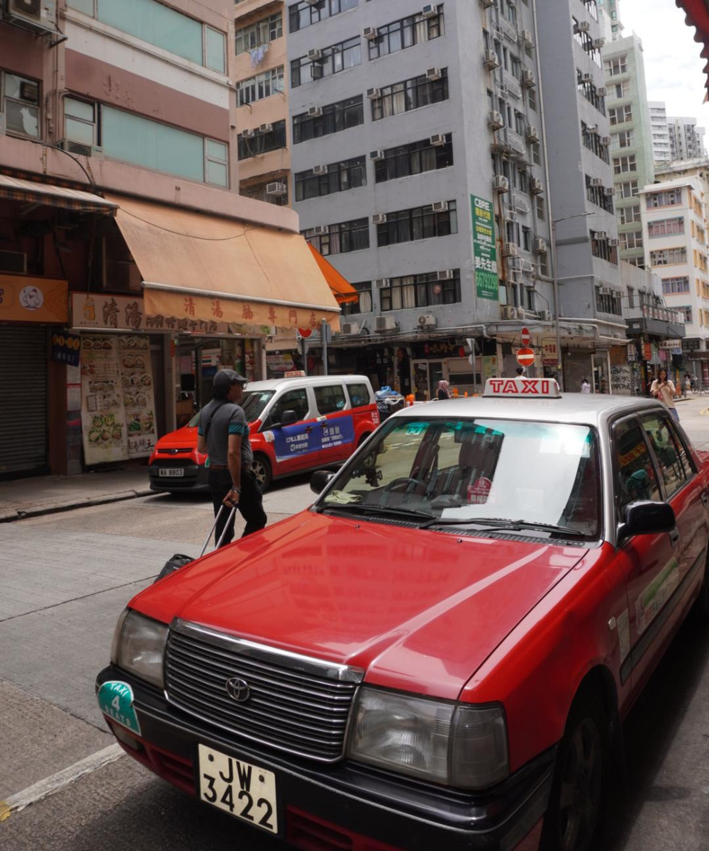 Táxi vermelho estacionado em uma rua movimentada, cercada por edifícios altos na Ásia.