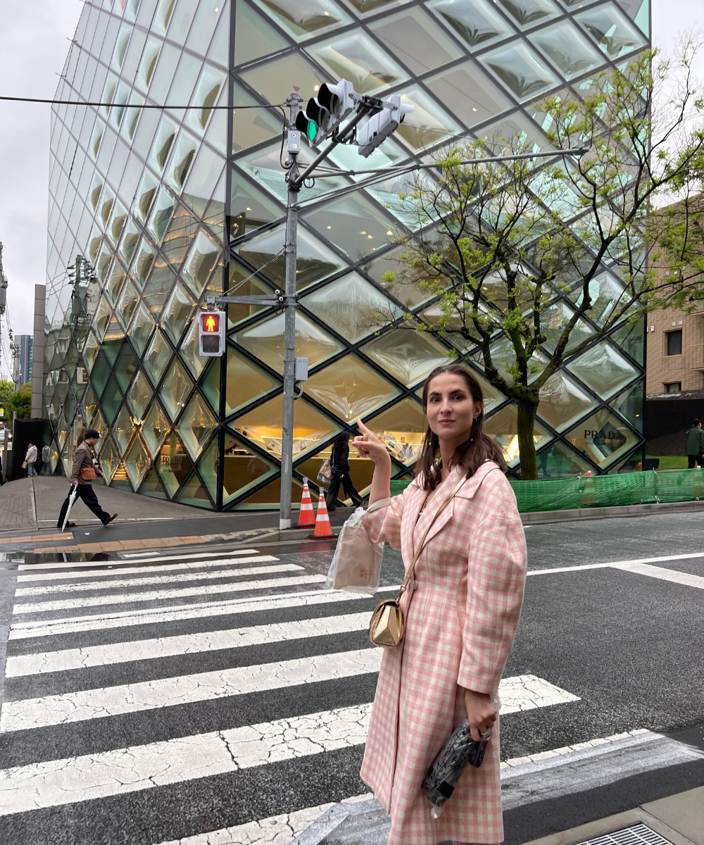 Mulher aponta para um moderno edifício de vidro em uma rua na Ásia.