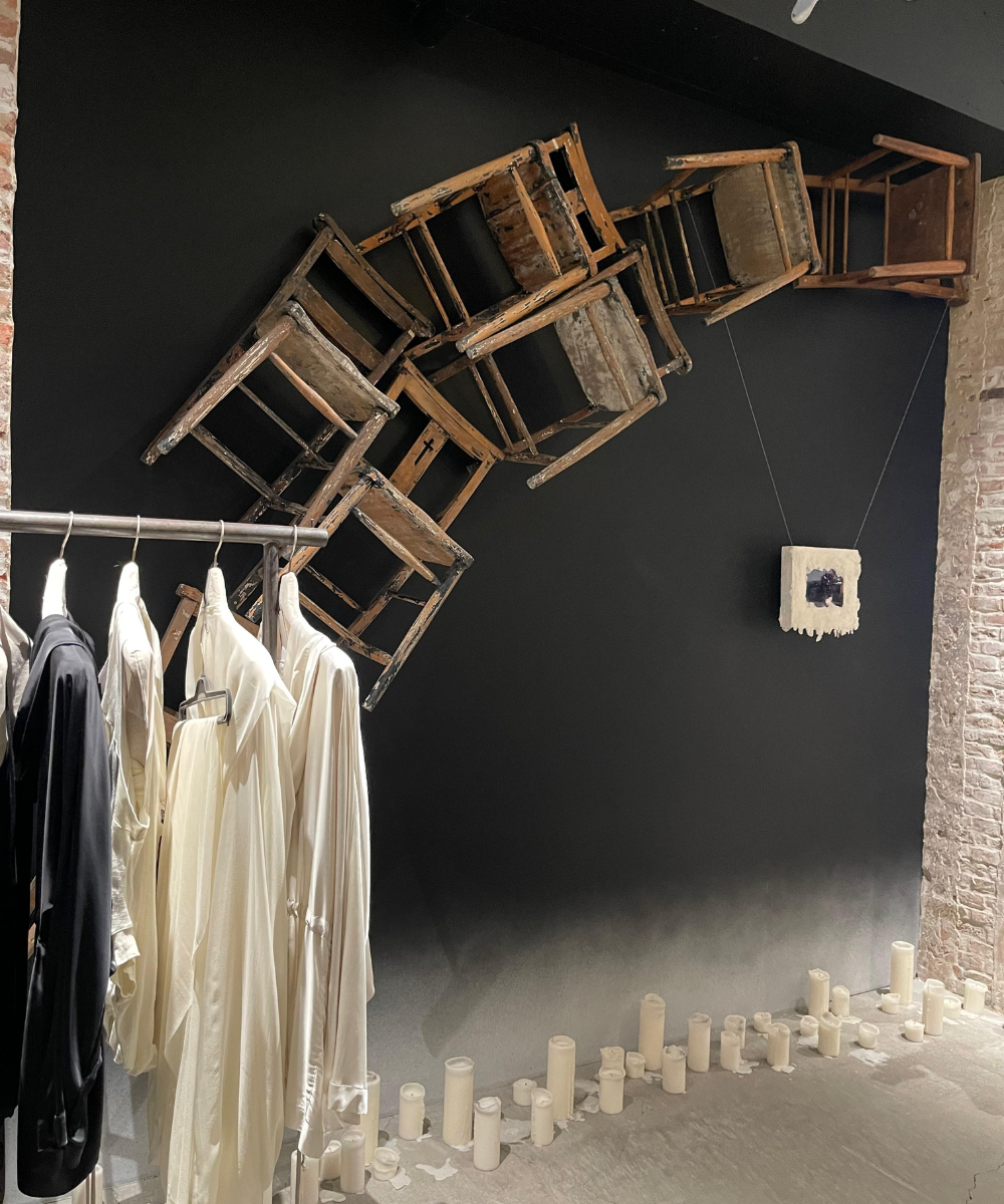 Cadeiras velhas em cascata na parede, roupas penduradas em um rack e velas no chão. Arte inspirada na Ásia.