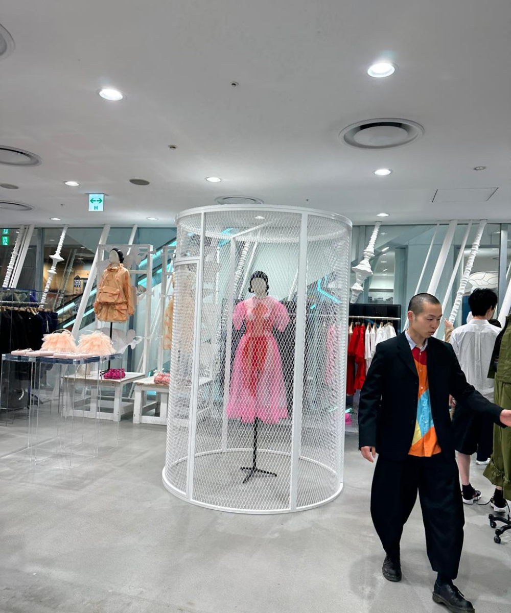Loja de moda contemporânea na Ásia com manequim de vestido rosa em gaiola metálica, cliente caminha ao lado.