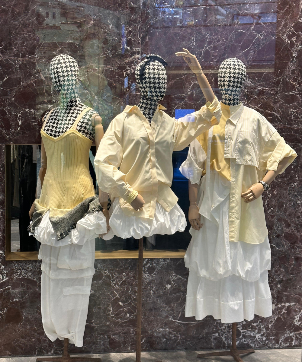 Manequins com roupas amarelas e brancas em uma vitrine de mármore.