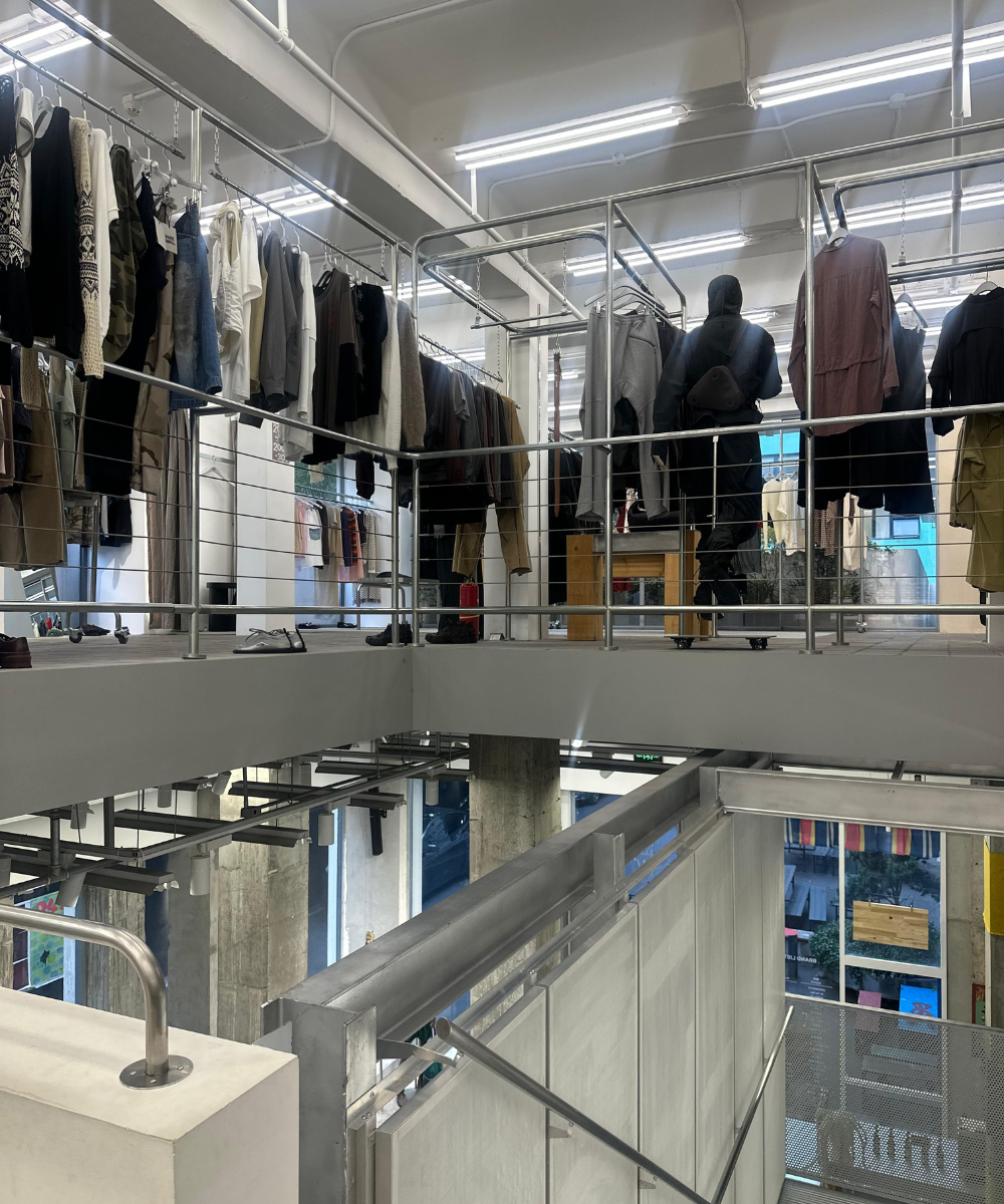 Loja moderna com roupas penduradas em cabides elevados; ambiente organizado e iluminado, possivelmente inspirado em estilo asiático.
