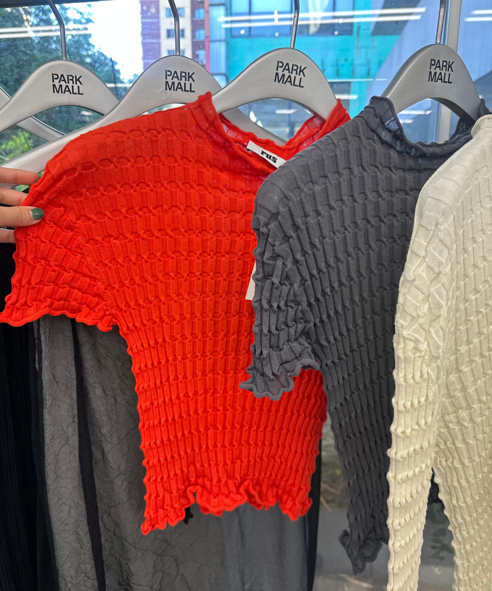 Blusas de tecido enrugado em vermelho, cinza e bege penduradas em cabides do Park Mall, Ásia ao fundo.