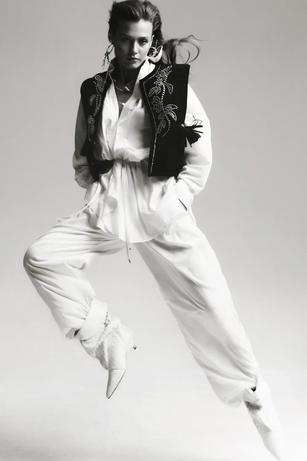 Modelo em pose dinâmica com roupa branca e colete bordado, estilo Isabel Marant.