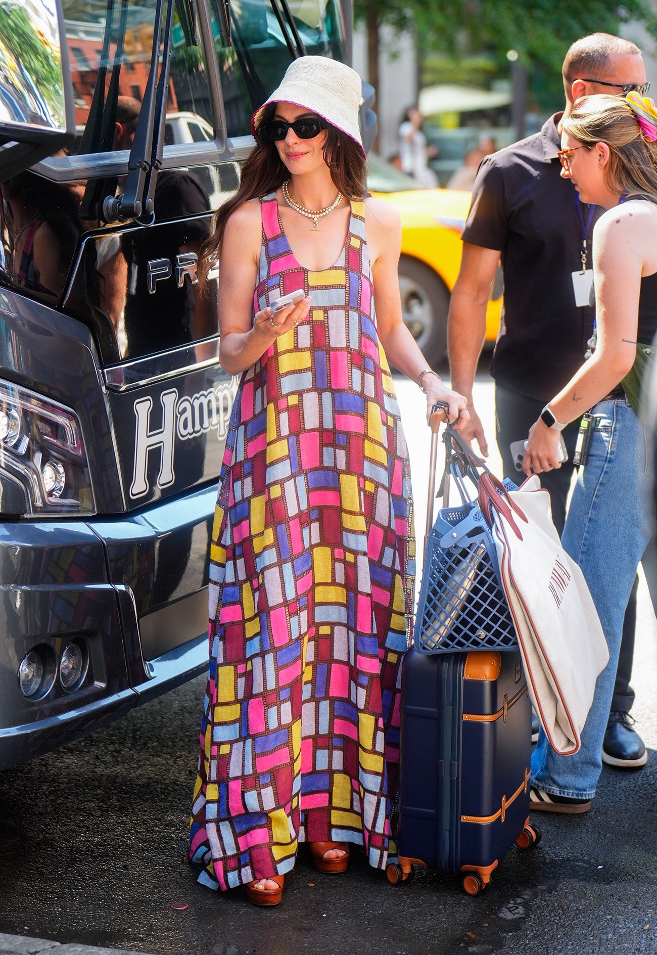 Pessoa com vestido colorido e chapéu ao lado de mala na rua. Contexto 