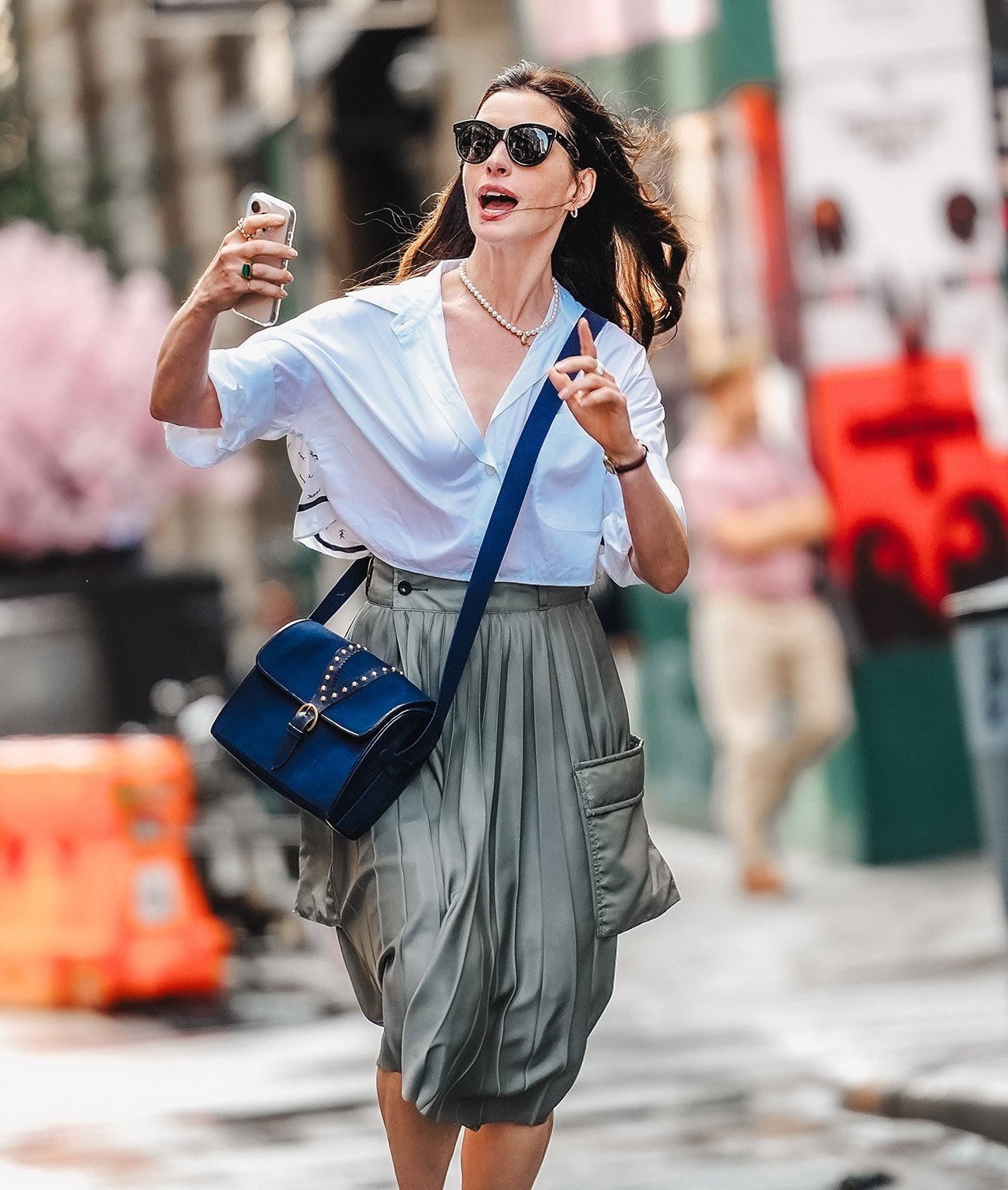 Mulher com camisa branca e saia cinza, usando óculos escuros e bolsa azul, caminhar urbano vibrante, elegância estilo moda.