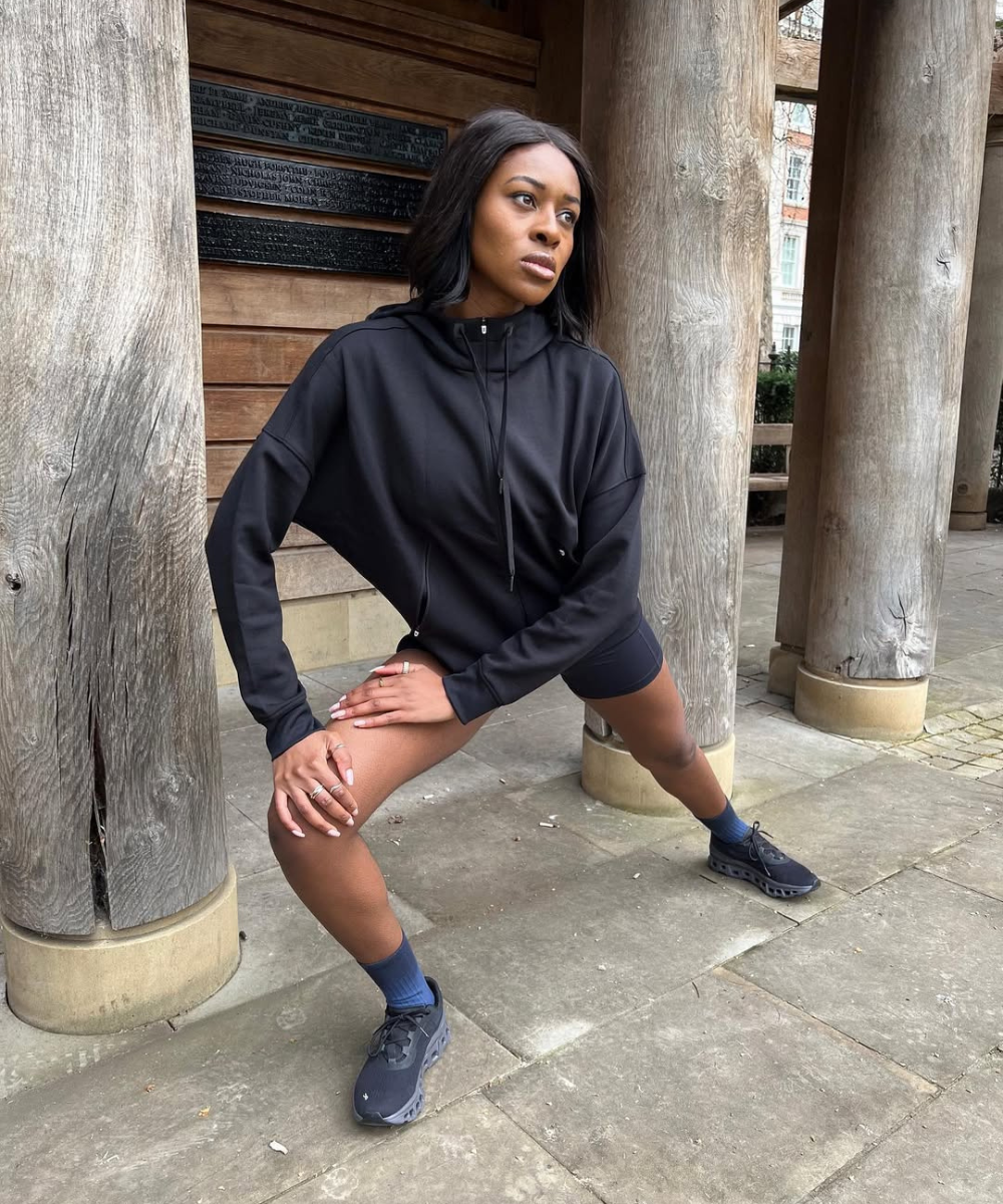 Pessoa usando moletom preto faz alongamento em ambiente externo rústico usa uma das melhores jaquetas para treinar no frio.