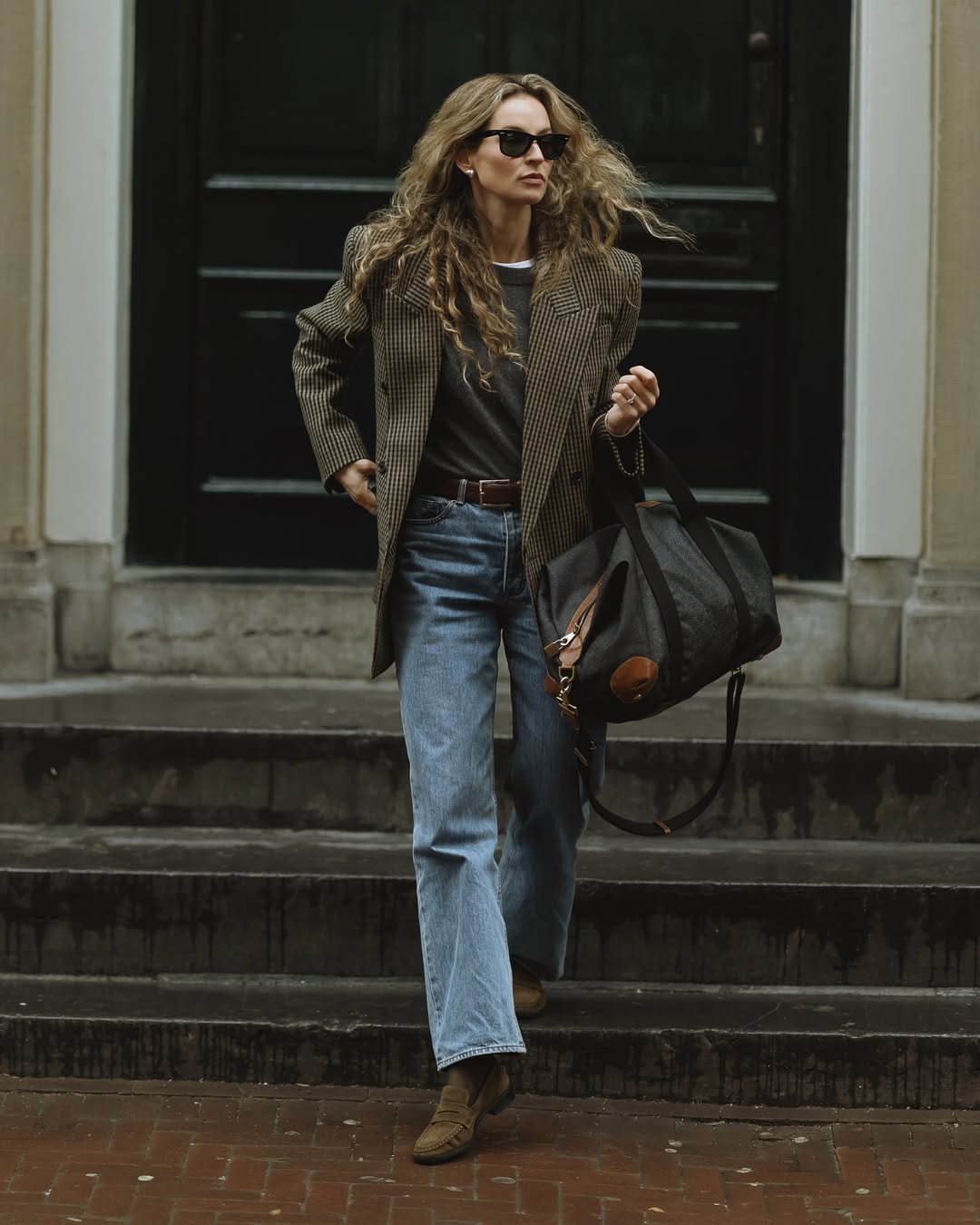 Pessoa com blazer xadrez, jeans e bolsa elegante, representando estilo casual e sofisticado para o trabalho.