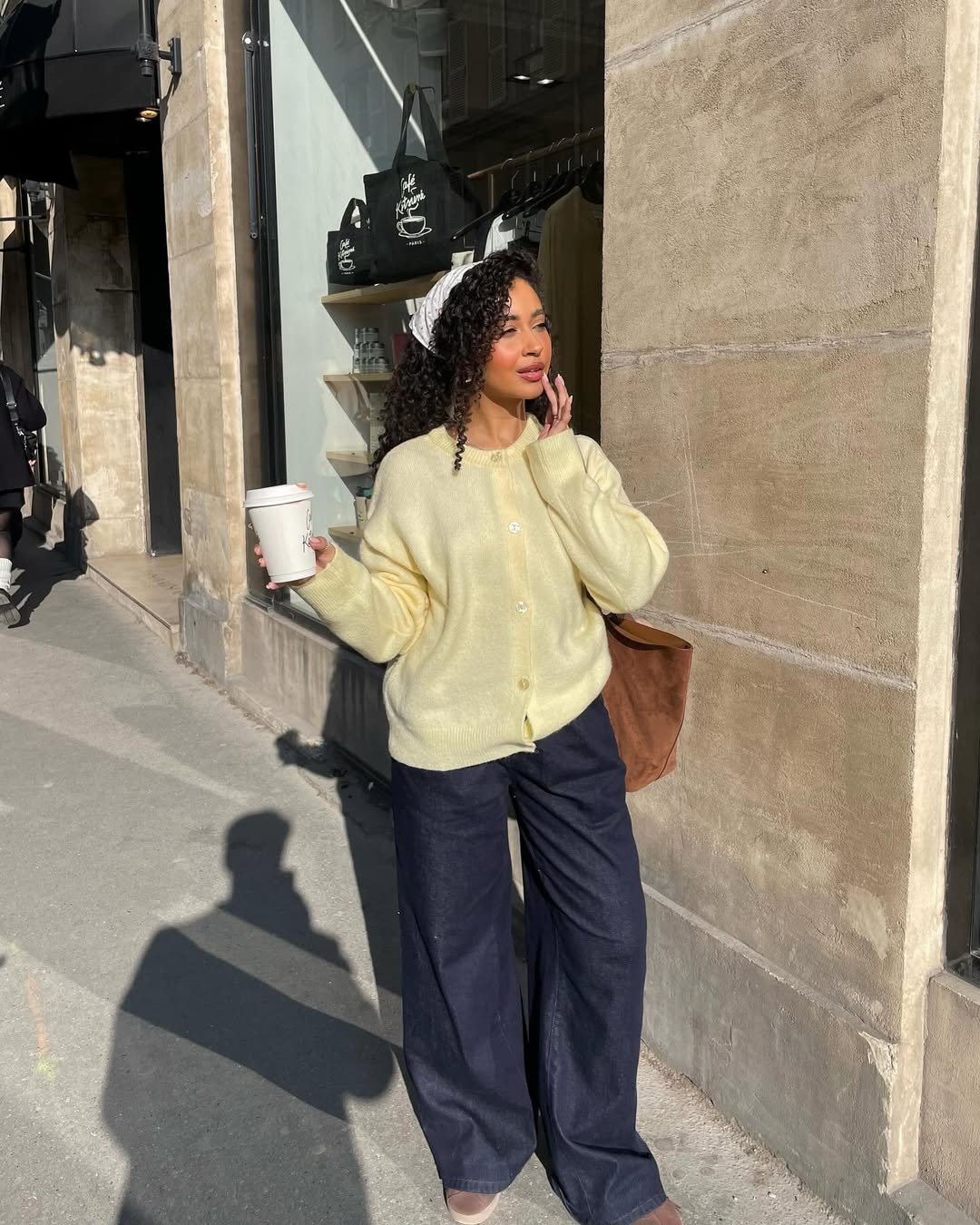 Pessoa vestindo suéter amarelo com lenço de renda nos cabelos, segurando café.