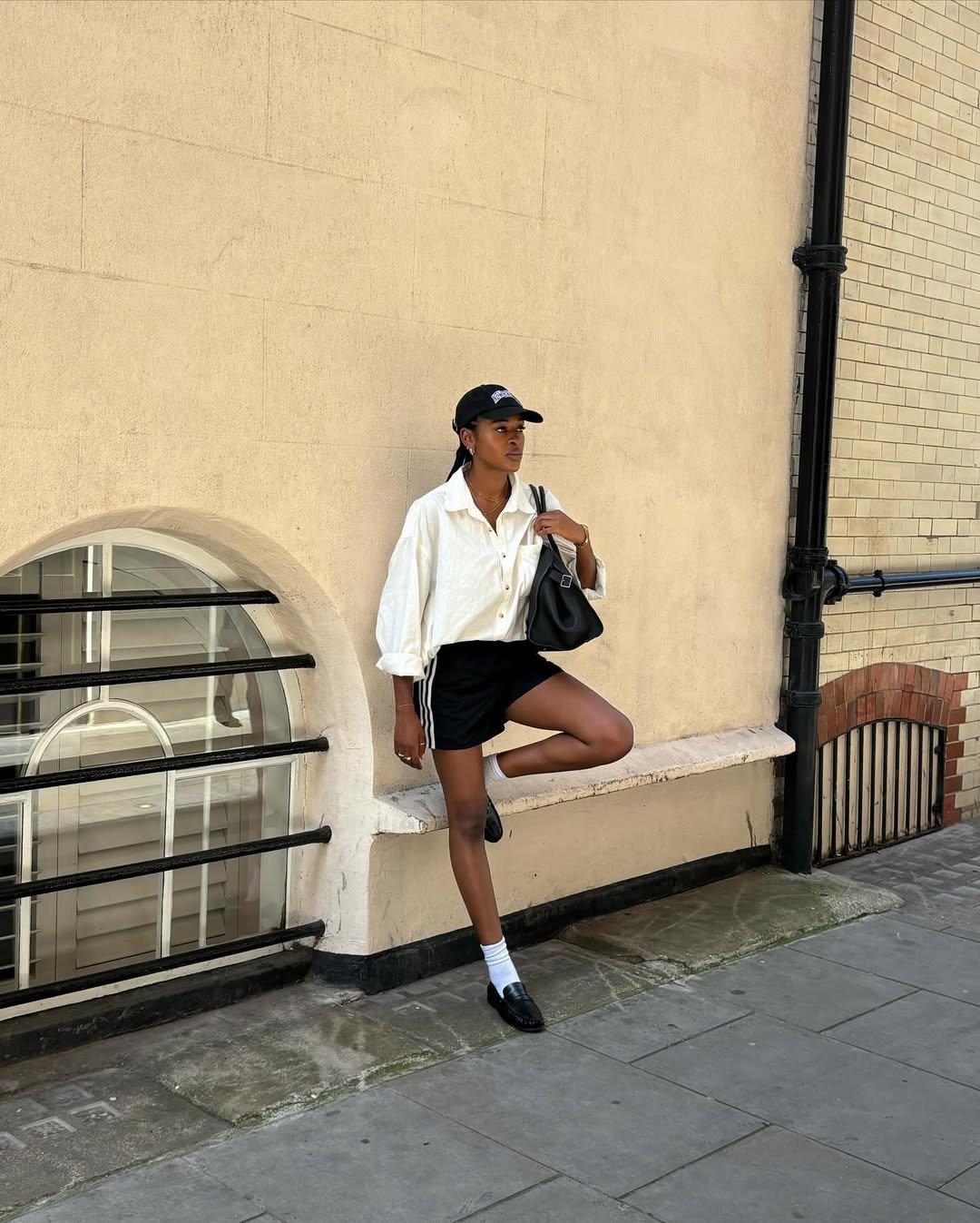 Pessoa usando camisa branca e shorts pretos, combinados com loafer feminino preto em ambiente urbano.