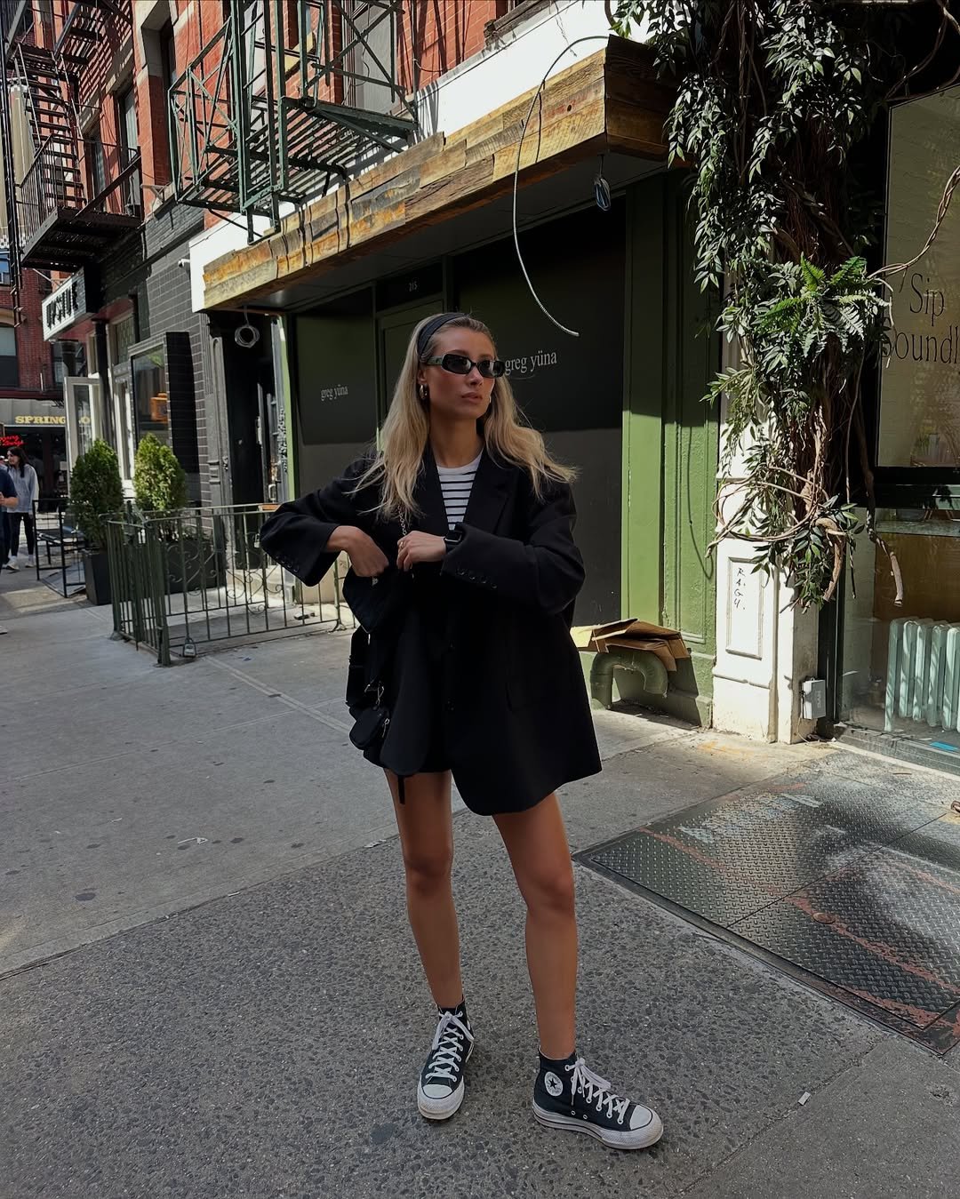 Mulher de blazer e all star preto em rua urbana ensolarada.