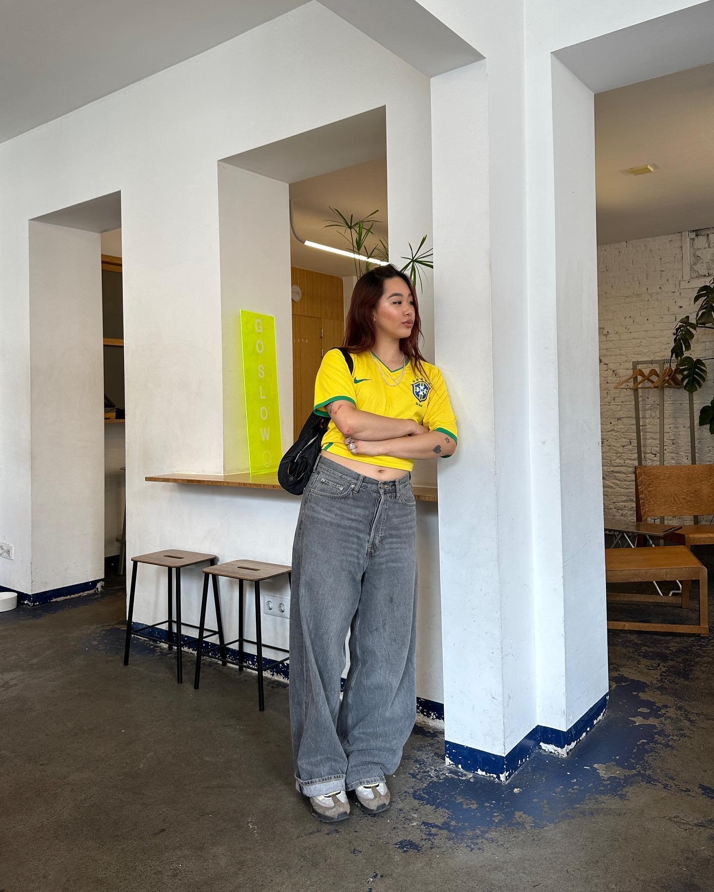 Pessoa usando camisa de time amarela, jeans largos e tênis em ambiente moderno.