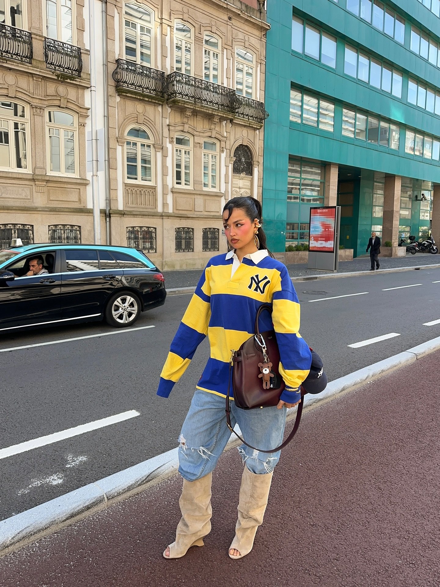 Pessoa usa blusa listrada azul e amarela, jeans rasgados e botas bege de salto alto.