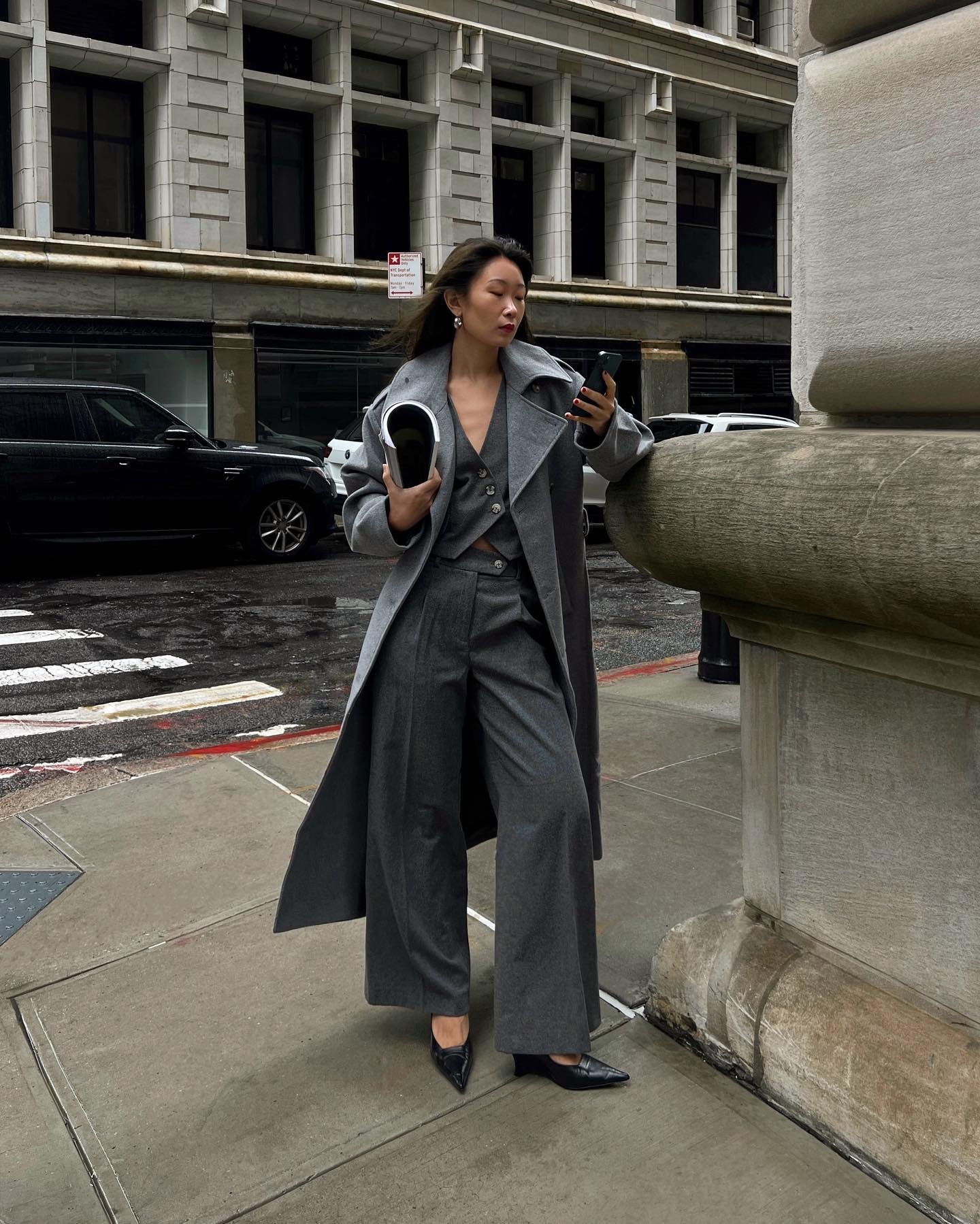 Pessoa em traje cinza elegante apoia-se em um corrimão, segurando sapato preto. Demonstra ideias de looks com salto anabela.