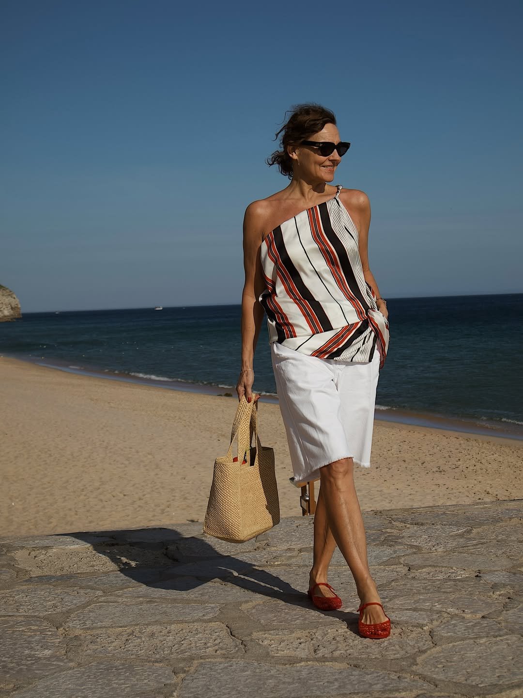 Pessoa em praia, usando blusa listrada e bermuda branca. Elegância em looks de calor estilosos.