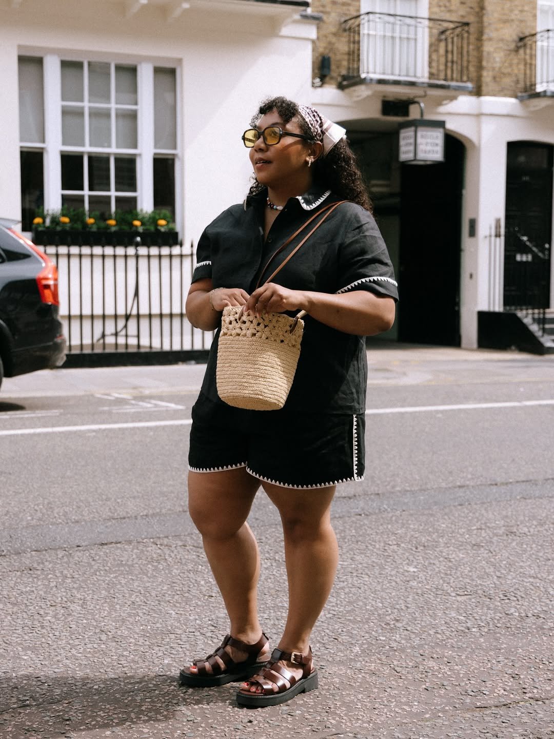 Pessoa em roupa preta casual na rua, usando sandálias e bolsa de palha; exemplo de looks de calor estilosos.
