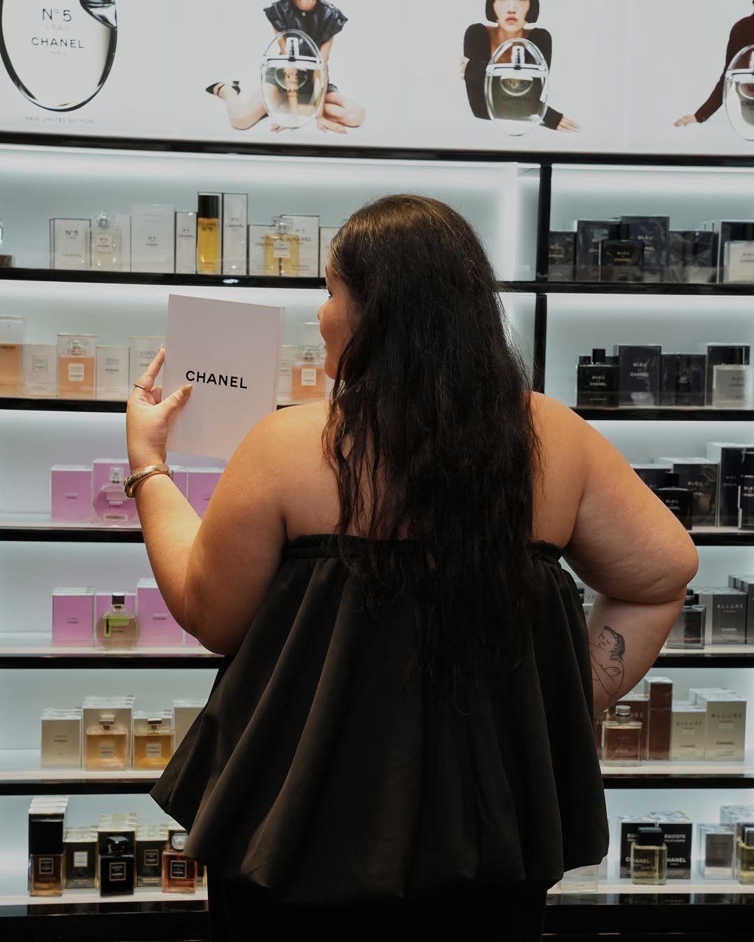 Pessoa segurando embalagem de perfume Chanel em frente a prateleira de fragrâncias diversas. Melhores perfumes