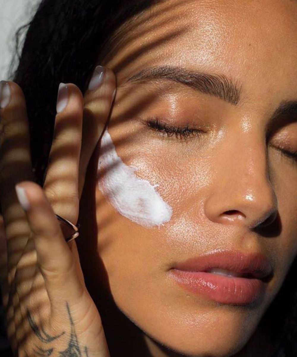 Pessoa aplicando creme no rosto iluminado, mostrando a prática de uso dos melhores produtos para pele oleosa