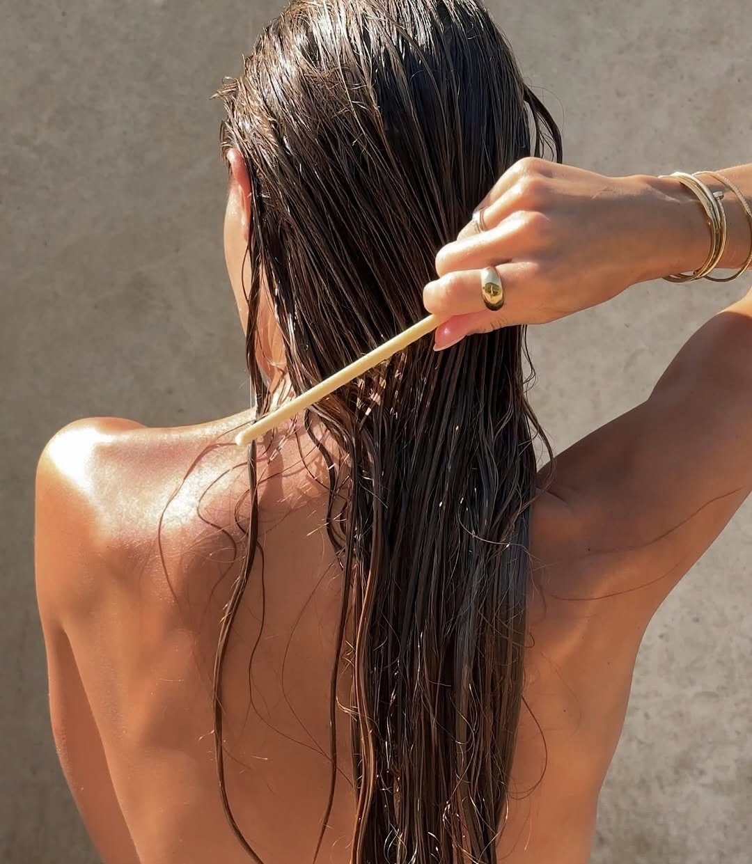 Pessoa penteando cabelos longos e molhados ao sol. Itens de cuidados com cabelo são essenciais num necessaire de inverno.